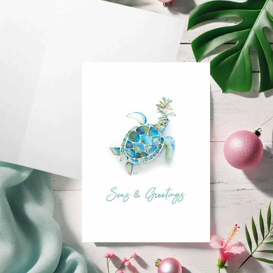 Flat lay of a beach Christmas cards featuring a watercolor sea turtle in shades of turquoise blue over a crisp white background. The words Seas & Greetings are set in trendy script type. Art and design by Victoria Grigaliunas of Do Tell A Bell a woman owned small business in Palm Beach Gardens, Florida.