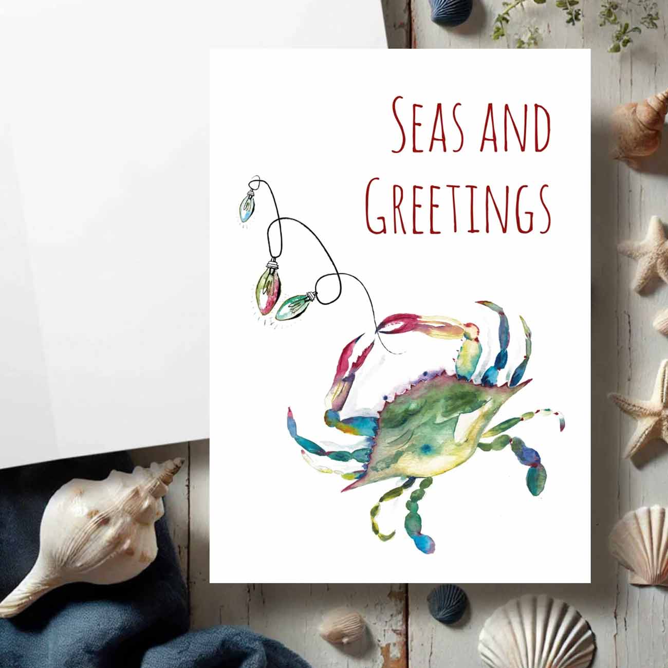 Flat lay of coastal Christmas cards designed with a watercolor blue crab by watercolor artist Victoria Grigaliunas of Do Tell A Belle a woman owned small business in South Florida