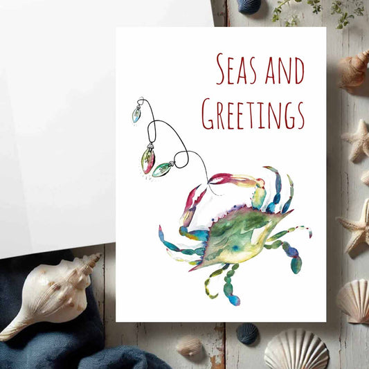 Flat lay of coastal Christmas cards designed with a watercolor blue crab by watercolor artist Victoria Grigaliunas of Do Tell A Belle a woman owned small business in South Florida