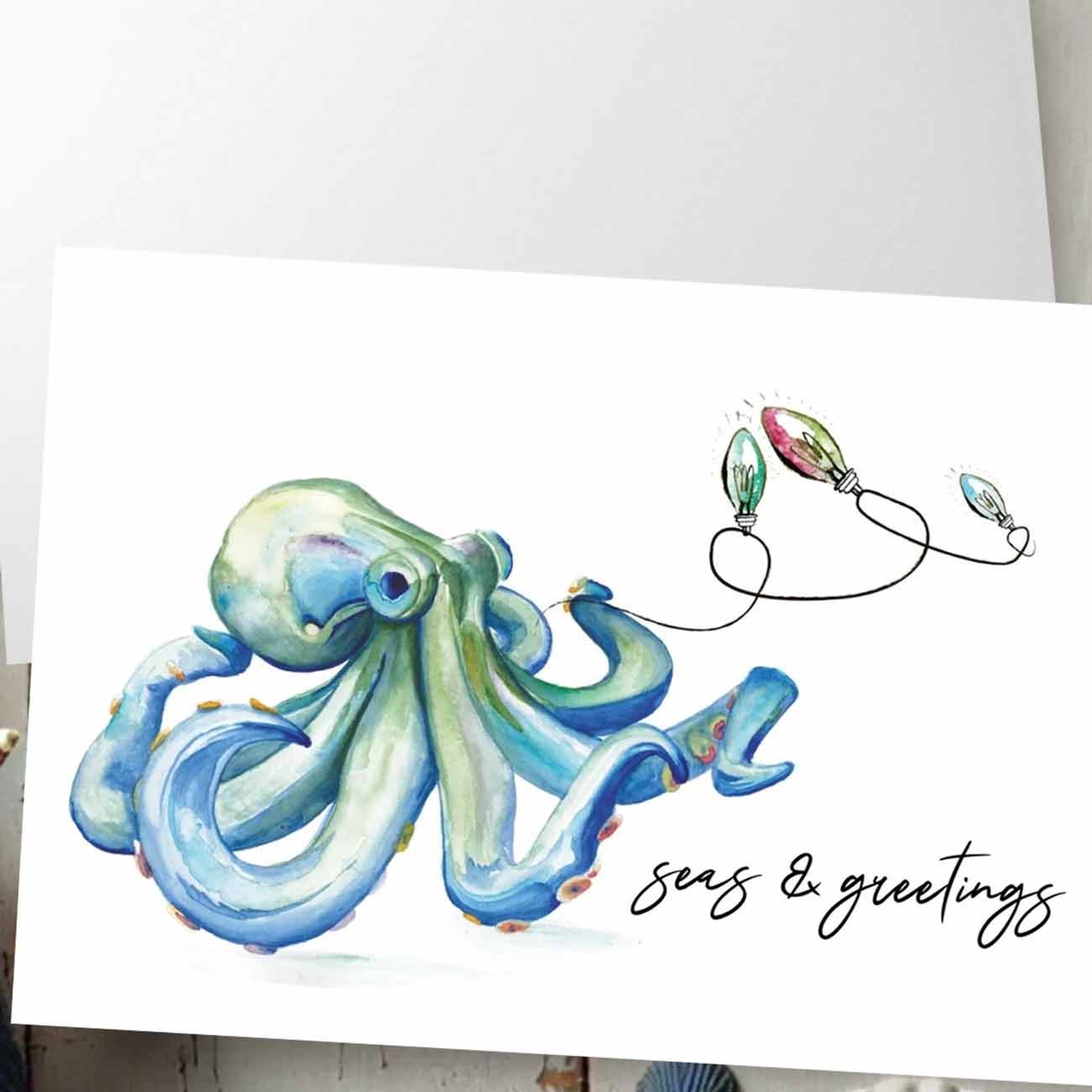 Zoomed in flat lay of nautical Christmas cards designed with a watercolor blue octopus and holiday lights by artist Victoria Grigaliunas of Do Tell A Belle a woman owned small business in Southern Florida.