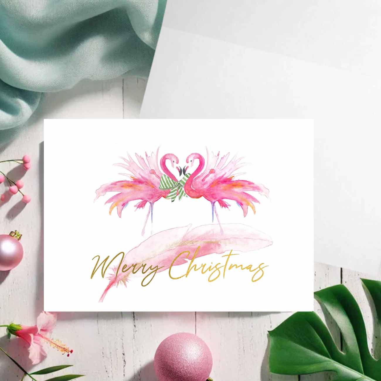 Flat lay of pink flamingo Christmas cards designed by Florida watercolor artist Victoria Grigaliunas of Do Tell A Belle a woman owned small business.