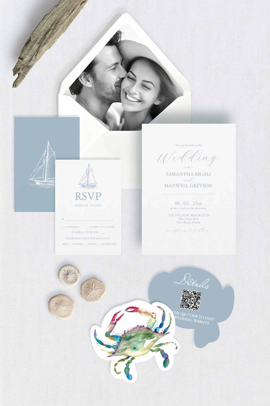 A styled flat-lay of a nautical-themed wedding invitation suite, featuring a white invitation card, a light blue RSVP card with a sailboat illustration, a die cut blue crab details card with qr-code, and a photo envelope liner inside a white envelope.