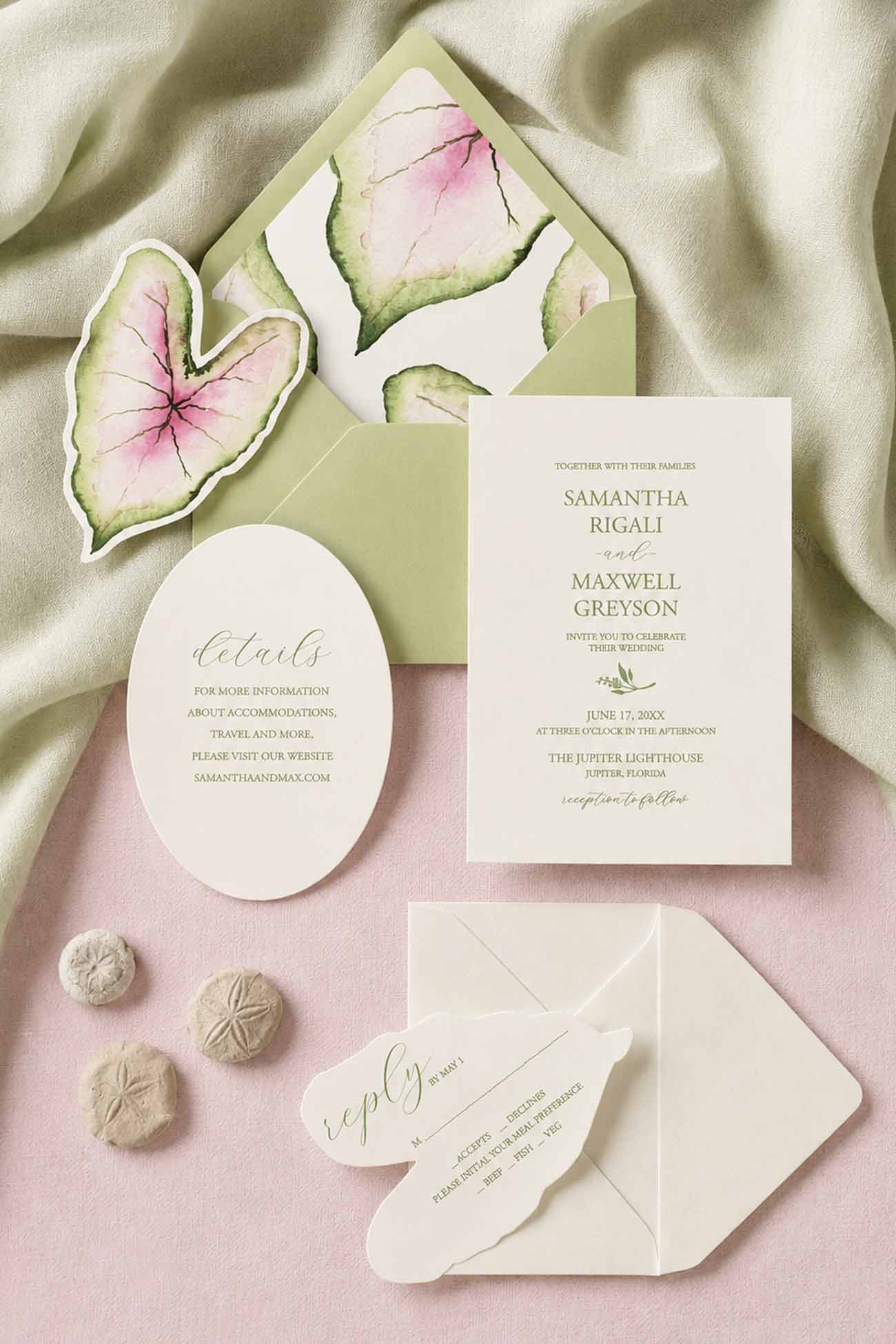 A styled flat-lay of a botanical pink and green wedding invitation suite printed on cream cardstock with green envelopes and caladium leaves envelope liner and laser cut rsvp cards. The set includes a invitation card, an oval details card, a caladium leaf-shaped RSVP card, and a green envelope.