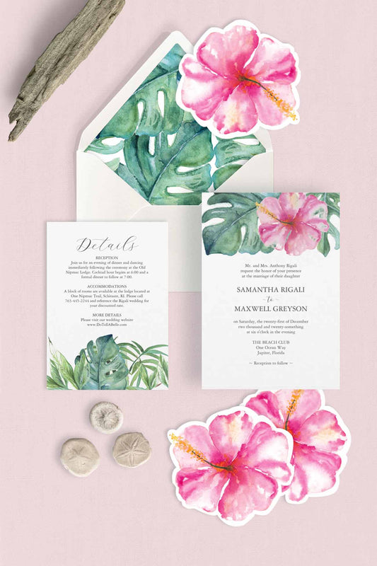 Tropical-themed wedding invitation suite with pink hibiscus flowers and green monstera leaves on a light pink background, styled with driftwood and sand dollars.